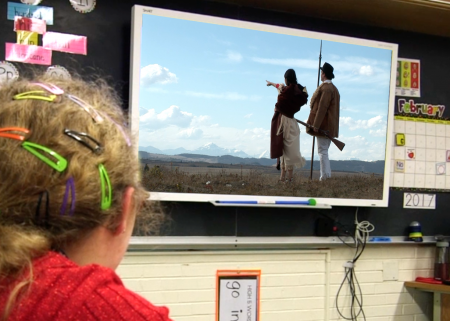Young girl watches Sacagawea video on screen in front of blackboard