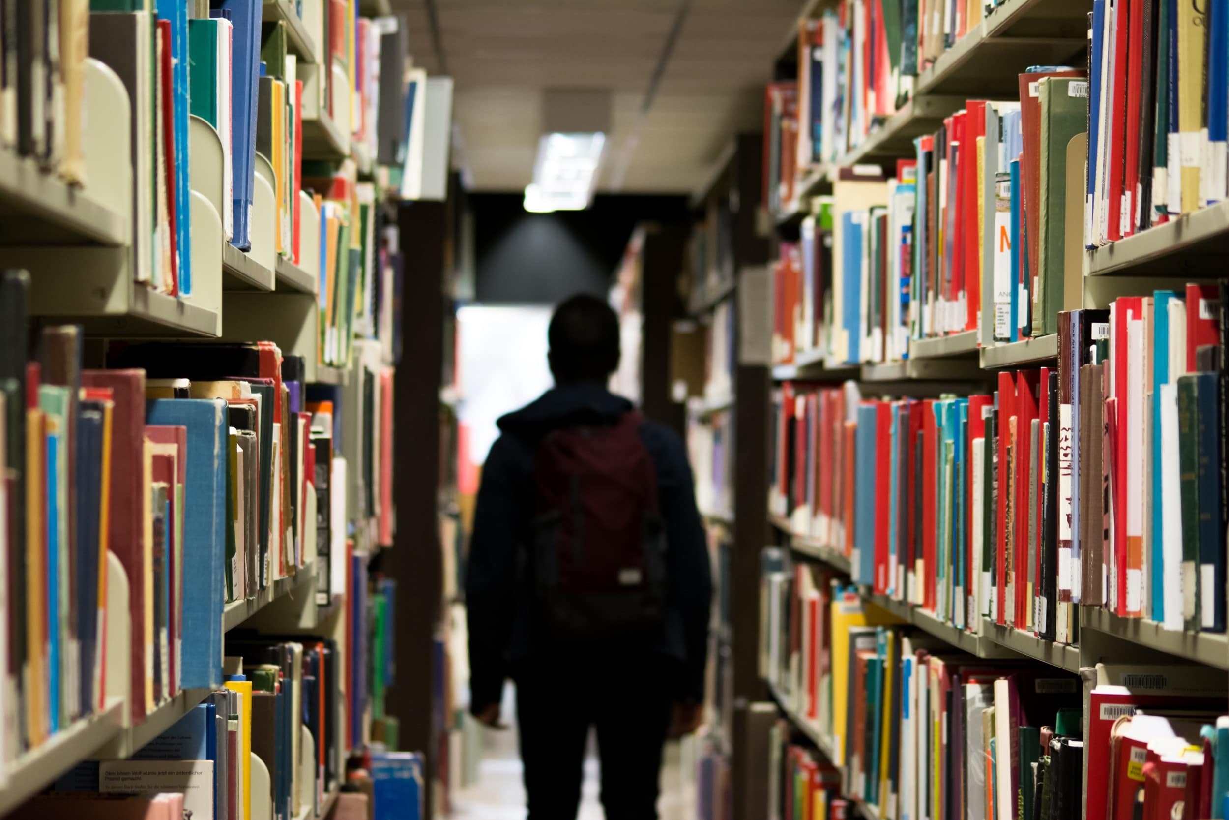 Student walking down an isle in a library full of books