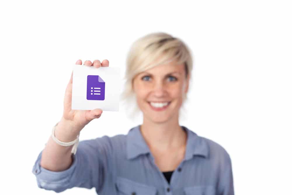 Woman smiling at the camera holding a card with the Google forms logo in her right hand
