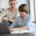 Parent instructing child on laptop while sitting at a coffee table