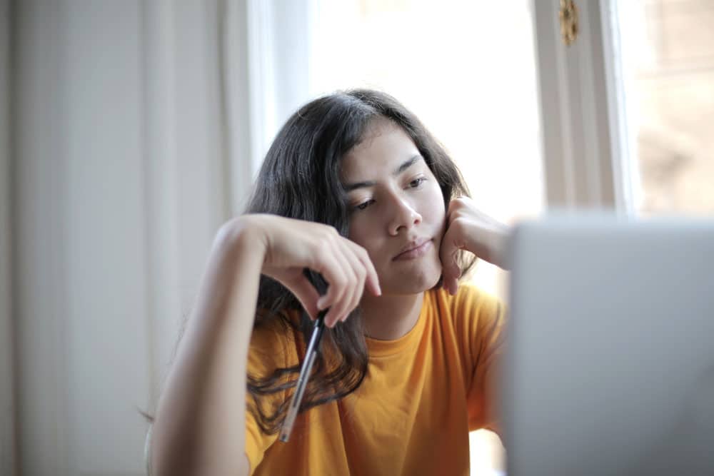 Girl in orange shirt studying on computer at home