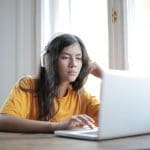 Girl in orange shirt using laptop at home