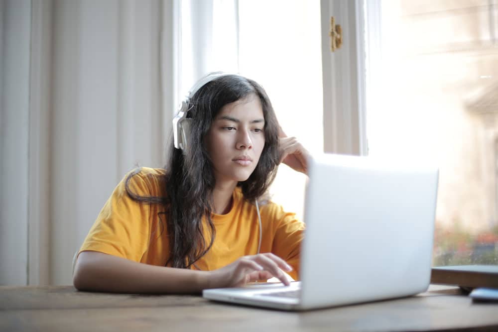 Girl in orange shirt using laptop at home