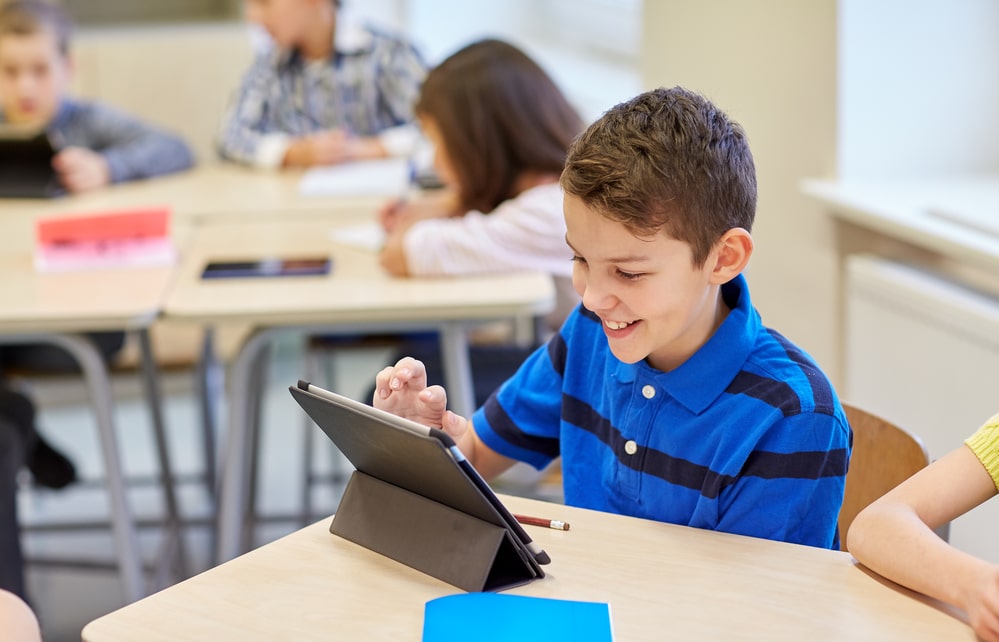 Three students work on tablet happily together in classroom