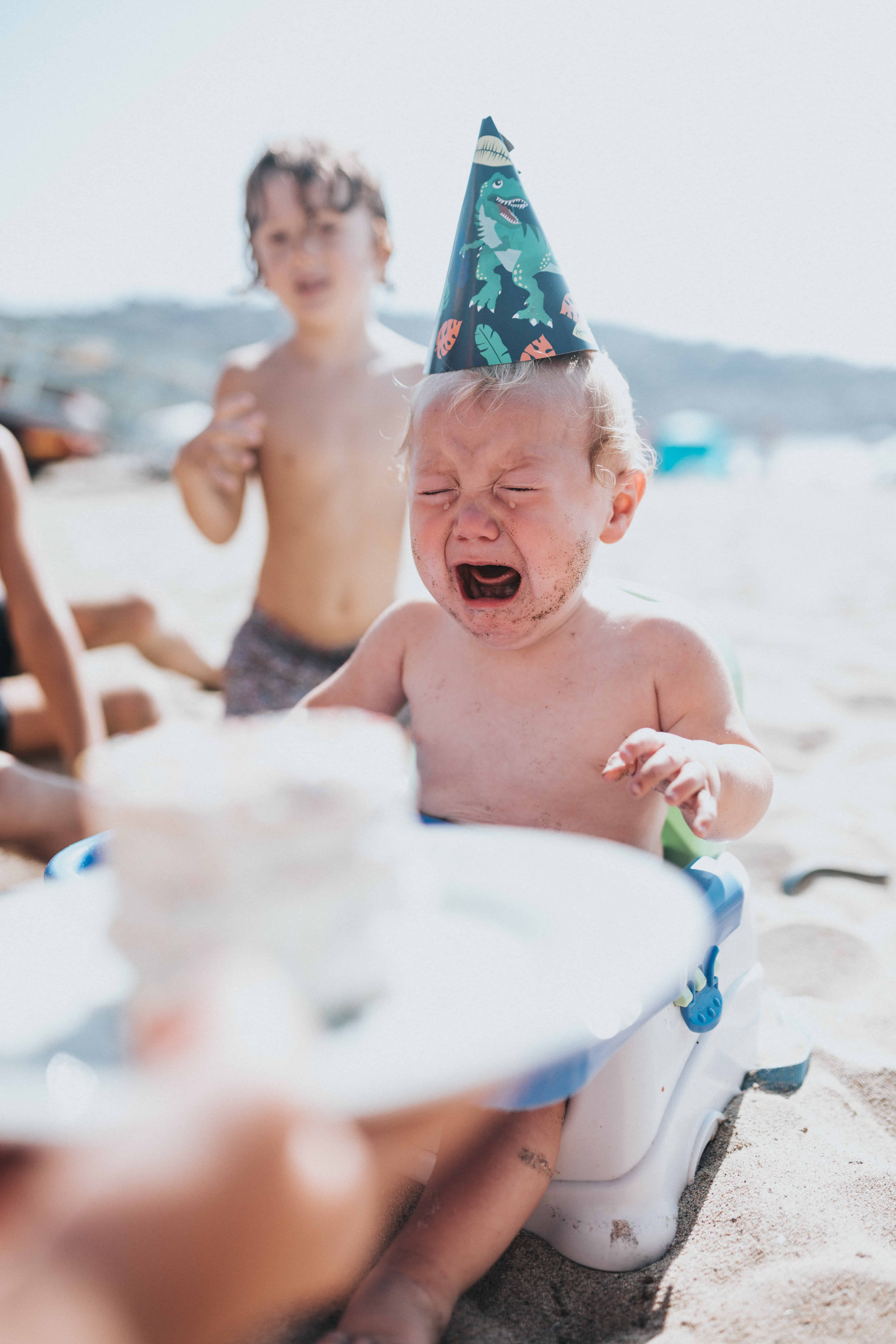 Child on a beach in a party hat crying