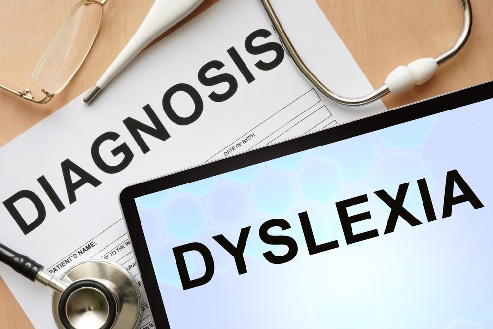 Top with the word "Dyslexia" written on the screen sitting on top of a paper with the word "Diagnosis" next to a stethoscope and thermometer.